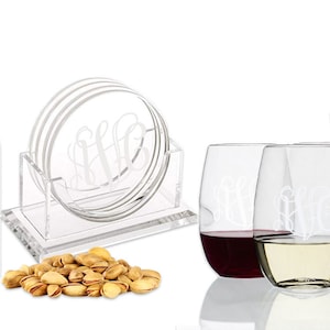 May include: Set of four clear glass coasters with a monogram design, a clear acrylic coaster holder, two clear glass stemless wine glasses with a monogram design, and a bowl of pistachios.