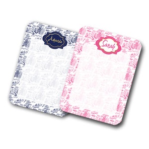 May include: Two personalized notepads with blue and pink floral borders. The notepad on the left has the name "Amanda" in gold lettering. The notepad on the right has the name "Sarah" in gold lettering.