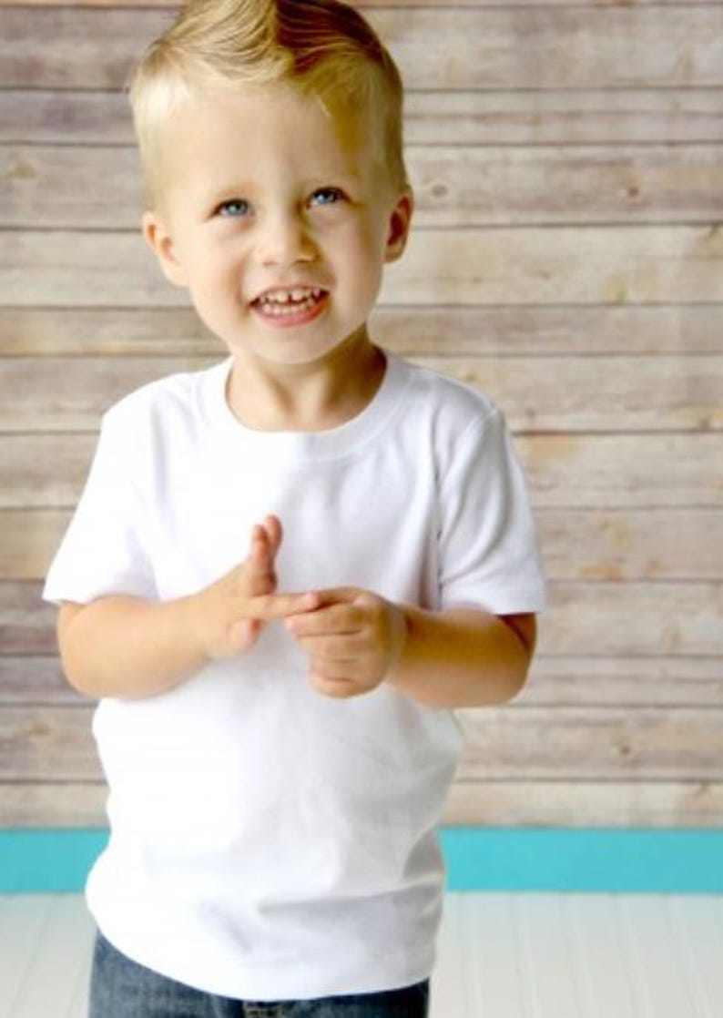 K&ouml;nnte beinhalten: Ein kleiner Junge tr&auml;gt ein wei&szlig;es T-Shirt und eine blaue Jeans. Er l&auml;chelt und schaut in die Kamera.