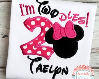May include: White t-shirt with pink and white polka dot number 2, pink bow, and black Minnie Mouse head. The text "I'm Two-dles!" is above the number and the name "Taelyn" is below.