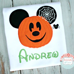 May include: White t-shirt with an orange pumpkin Mickey Mouse face, black ears, and a black spider web with a black spider. The name "ANDREW" is embroidered in green below the pumpkin face.