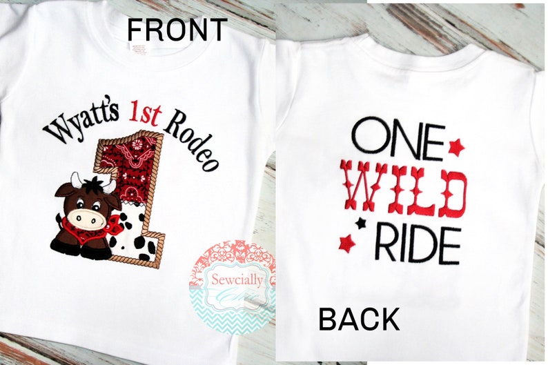 K&ouml;nnte beinhalten: Wei&szlig;es T-Shirt mit einem roten und schwarzen Stickmotiv auf der Vorderseite. Das Motiv zeigt eine Comic-Kuh und den Text "Wyatt's 1st Rodeo". Die R&uuml;ckseite des Shirts tr&auml;gt den Text "ONE WILD RIDE" in Rot und Schwarz.