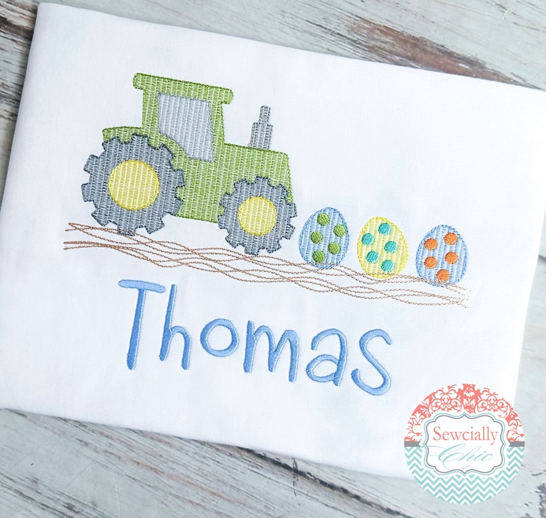 May include: Green tractor pulling a line of colorful Easter eggs with the name Thomas embroidered in blue below.