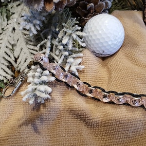 Puede incluir: Un brazalete de cuentas rosa y negro con un cierre plateado y un cordón negro. El brazalete está sobre una superficie de tela beige.