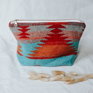 May include: A turquoise, red, orange, and gray patterned zippered pouch. The pouch is made of a soft, fuzzy fabric.
