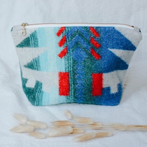 May include: A white zippered pouch with a colorful geometric pattern in shades of blue, green, and red. The pattern resembles a stylized mountain range.