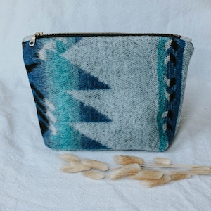 May include: A blue and white patterned zippered pouch with a geometric design. The pouch is made of a soft, textured fabric.