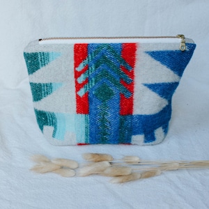 May include: A white zippered pouch with a colorful geometric pattern in shades of red, blue, and green. The pattern resembles a Native American design.