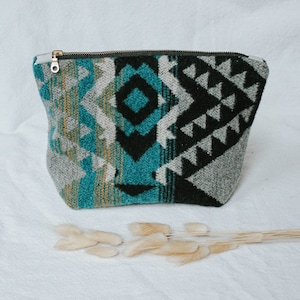 May include: A teal, black and grey patterned zippered pouch with a geometric design.
