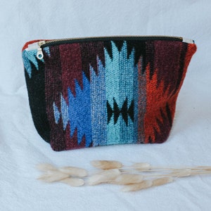 May include: A colorful zippered pouch with a geometric pattern in shades of blue, red, and black. The pouch is made of a woven fabric and has a zipper closure.