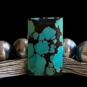 May include: A rectangular turquoise stone with dark brown matrix patterns, centered on a multi-strand silver liquid chain necklace featuring polished round silver beads on each side of the central stone.