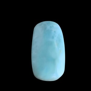 May include: A polished, elongated oval-shaped Larimar gemstone featuring a smooth, cabochon surface. The stone displays a vibrant sky-blue color with marbled white patterns and subtle cloud-like inclusions throughout its opaque, rounded structure.