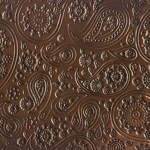 May include: A detailed close-up of a brown paisley pattern. The design features intricate floral and teardrop shapes, creating a textured, embossed effect. The color is a warm, earthy brown, with variations in tone that highlight the pattern's depth.