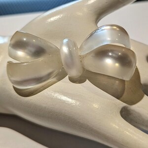 Könnte beinhalten: Eine weiße Plastik-Schleifenbrosche mit Perlmutt-Finish.