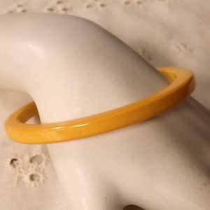 May include: A yellow plastic bangle bracelet. The bracelet is smooth and shiny.