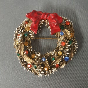 May include: A gold-toned Christmas wreath brooch with a red enamel bow and colorful rhinestones.