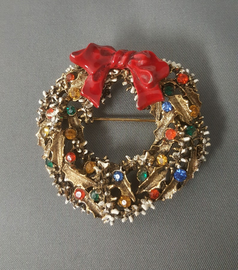 May include: A gold-toned Christmas wreath brooch with a red enamel bow and colorful rhinestones.
