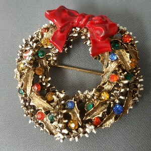 May include: A gold-tone Christmas wreath brooch with a red enamel bow and colorful rhinestones.