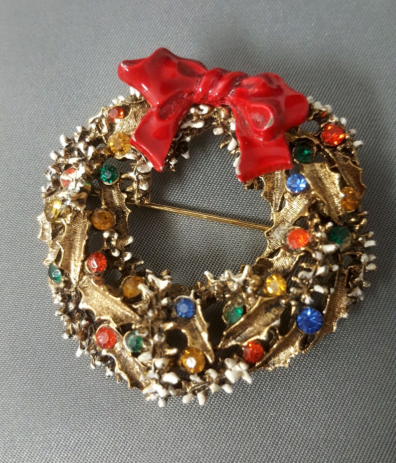 May include: A gold-tone Christmas wreath brooch with a red enamel bow and colorful rhinestones.