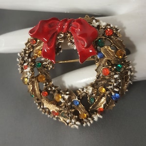 May include: A gold-tone Christmas wreath brooch with a red enamel bow and colorful rhinestones.