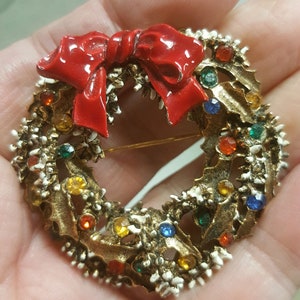 May include: A gold-toned Christmas wreath brooch with a red bow and colorful rhinestones.