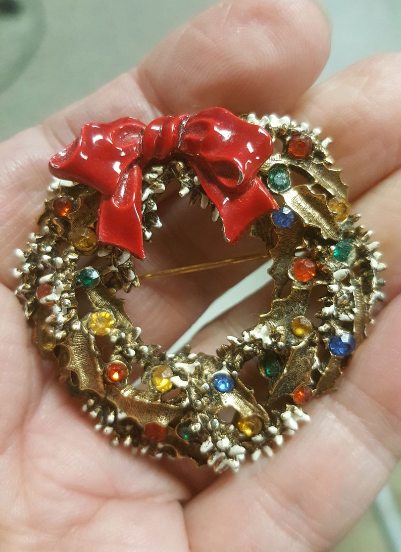 May include: A gold-toned Christmas wreath brooch with a red bow and colorful rhinestones.