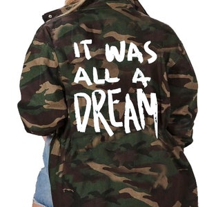 May include: A green, brown and tan camouflage jacket with a white graphic on the back that says "It Was All A Dream".