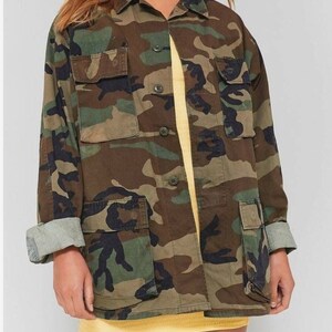 May include: A green, brown and black camouflage jacket with a button-up front and multiple pockets.