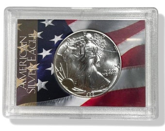 May include: A silver American Silver Eagle coin in a clear protective case. The coin features a walking Liberty design. The case has a backdrop of the American flag and the text "AMERICAN SILVER EAGLE".