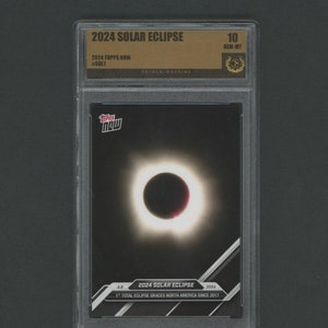 May include: A graded trading card featuring a photo of the 2024 solar eclipse. The card is graded GEM-MT 10 by Golden Grading. The card is from the 2024 Topps Now series and is numbered #SOL1.