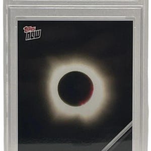 May include: A Topps Now trading card featuring a depiction of the 2024 Solar Eclipse. The card is encased in a protective holder and graded as a 10 GEM-MT. The card's design shows the eclipse with a black center and a bright halo.