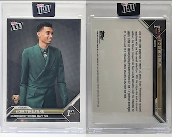 Op de afbeelding: Een verzamelkaart met Victor Wembanyama, een basketbalspeler, in een groen pak. De kaart is uit de serie Topps Now 2023 en is gemarkeerd met "1st Pick".