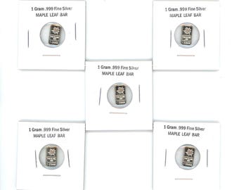 Può includere: Cinque lingotti d'argento fino .999 da 1 grammo Maple Leaf. Ogni lingotto è racchiuso in una scheda bianca con il testo "1 Gram .999 Fine Silver MAPLE LEAF BAR". I lingotti presentano un design a foglia d'acero e la scritta "1 GRAM".