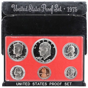 Op de afbeelding: Een Amerikaans Proof-set met munten uit 1975. De set bevat een halve dollar, een kwart dollar, een dime, een nikkel en een cent. De munten zijn gerangschikt in een rode en witte display case met de woorden "United States Proof Set" gedrukt op de bodem.