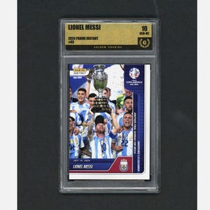May include: A graded Lionel Messi 2024 Panini Instant card. The card features Messi holding a trophy with teammates, celebrating a victory. The card is graded 10 GEM-MT by Golden Grading.