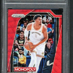Op de afbeelding: Een beoordeelde Victor Wembanyama 2024 Panini Prizm Red Wave #73 basketbalkaart. De kaart toont een speler in een San Antonio Spurs-uniform met een basketbal. De kaart is ingekapseld in een beschermende houder met de tekst "VICTOR WEMBANYAMA" en "MONOPOLY".
