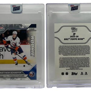 May include: A hockey trading card featuring Matthew Schaefer of the New York Islanders in a clear protective case. The card is labeled "Rookie" and includes the text "Youngest D-Man in NHL history to 25 career points."