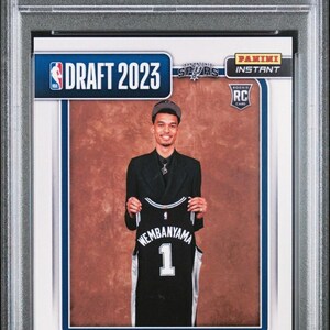 May include: A 2023 Panini Instant Victor Wembanyama Draft Night trading card graded PSA Mint 9. The card features a photograph of Victor Wembanyama holding a black San Antonio Spurs jersey with the number 1, encased in a clear protective plastic slab.