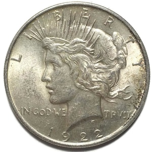 May include: A silver Peace Dollar coin with the year 1922 inscribed on the bottom. The coin features a profile of a woman with flowing hair and the words "LIBERTY" and "IN GOD WE TRUST" inscribed around the edge.