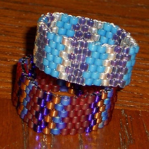 May include: Two beaded rings stacked on top of each other. The top ring is blue, white, and purple. The bottom ring is red, orange, and purple.