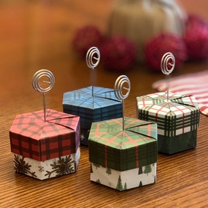 May include: Four hexagonal gift boxes with plaid patterns in red, green, blue, and white. Each box has a silver wire photo clip attached to the top.
