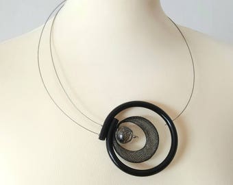 May include: A black necklace with a large, circular pendant. The pendant features a black mesh design with a silver sphere in the center.