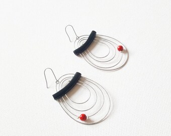 May include: A pair of silver wire earrings with black curved accents and red beads. The earrings are shaped like ovals with multiple wire circles.