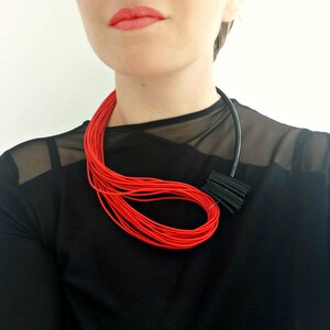 May include: A red and black statement necklace with a geometric design. The necklace is made of thin, layered cords and a black plastic piece.