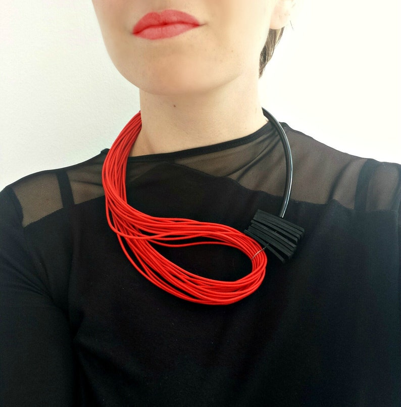 May include: A red and black statement necklace with a geometric design. The necklace is made of thin, layered cords and a black plastic piece.