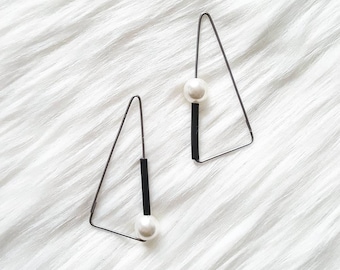 May include: A pair of black triangle earrings with a white pearl dangling from each earring.