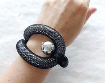 Op de afbeelding: Een zwarte mesh armband met een zilveren bol in het midden. De armband is flexibel en kan worden aangepast aan verschillende polsmaten.