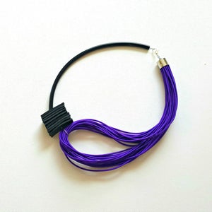 May include: A modern necklace featuring a black, curved band and a cluster of vibrant purple cords. A black, textured square detail is attached to the band. The necklace is secured with a silver clasp, creating a striking contrast.
