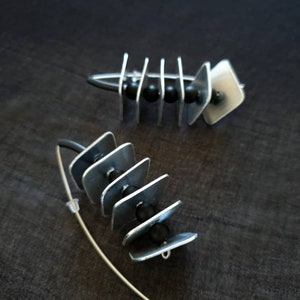 May include: A pair of silver earrings with black beads and geometric shapes. The earrings are made of metal and have a modern design.