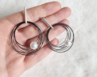 May include: A pair of black wire earrings with a pearl accent. Each earring features multiple wire loops forming a circle.